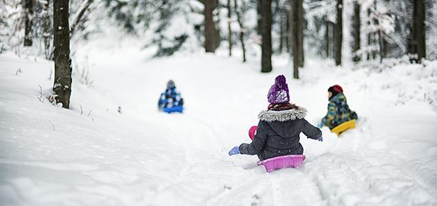 Three children sledding in the snow outside