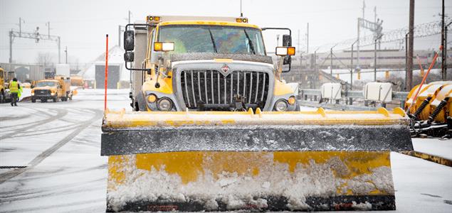 A yellow PennDOT plow truck drives through winter weather.